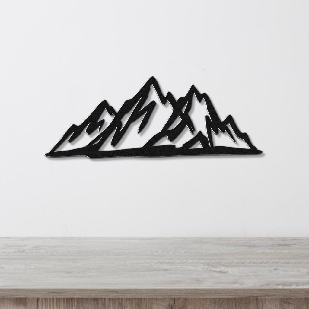 Black metal mountain silhouette wall art with layered peaks, mounted on a white wall above a light wood surface.