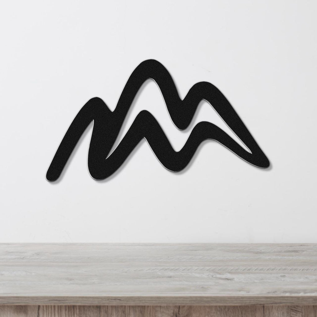 Black metal wall art with a wavy mountain silhouette, mounted on a white wall above a light wood surface.