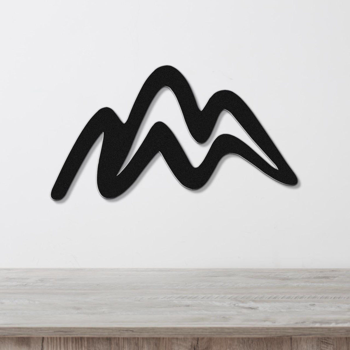 Black metal wall art with a wavy mountain silhouette, mounted on a white wall above a light wood surface.