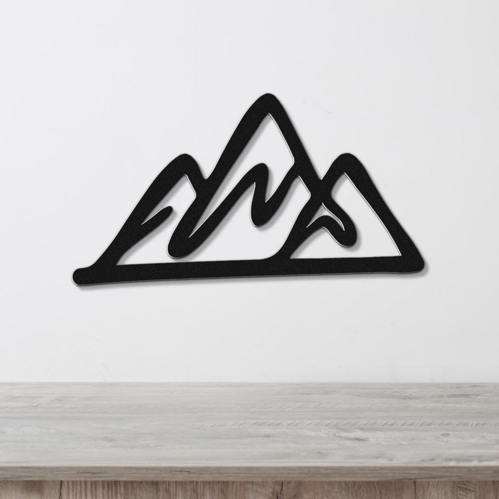 Black metal mountain silhouette wall art with layered peaks, mounted on a white wall above a light wood surface.