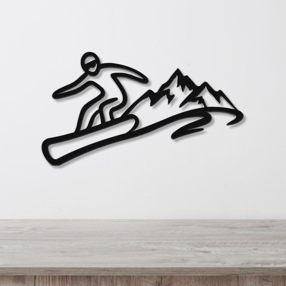 Black metal wall art featuring a snowboarder silhouette in dynamic motion above a mountain range, mounted on a white wall above a wooden counter.