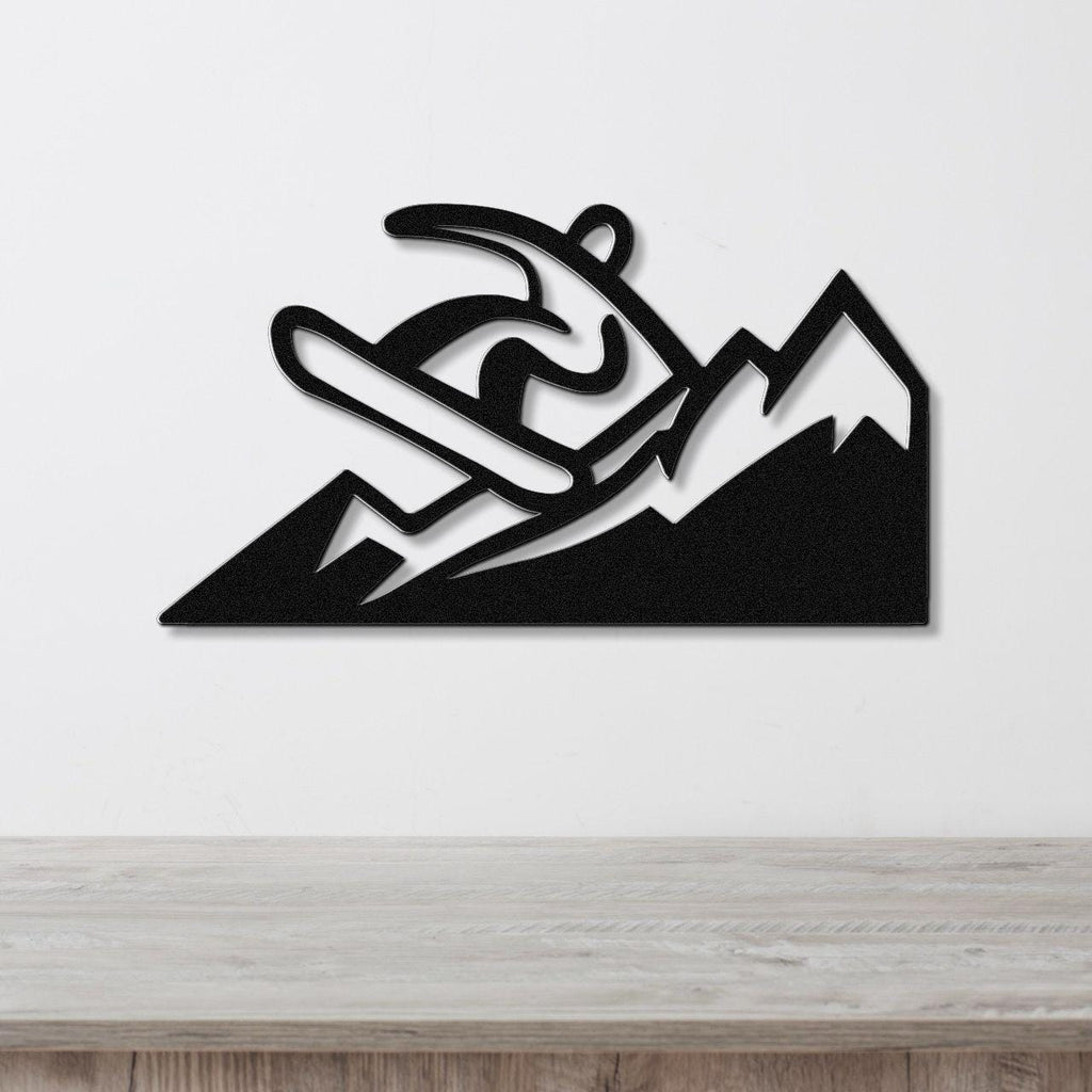 Black metal wall art featuring a snowboarder silhouette in motion above mountain peaks, mounted on a white wall above a wooden counter.