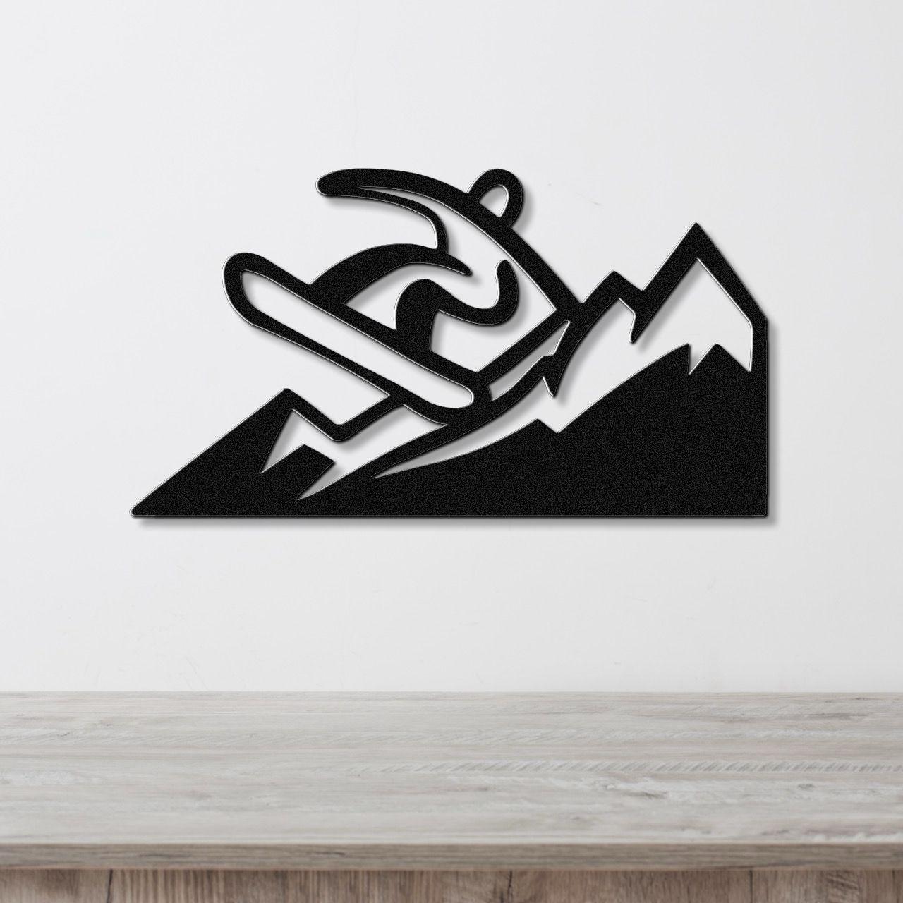 Black metal wall art featuring a snowboarder silhouette in motion above mountain peaks, mounted on a white wall above a wooden counter.
