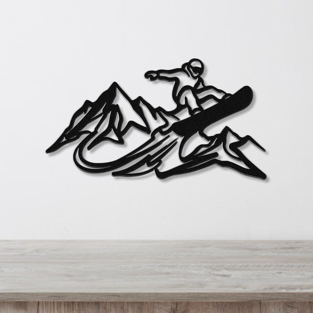 Black metal wall art featuring a snowboarder silhouette above mountain peaks, mounted on a white wall above a wooden counter.