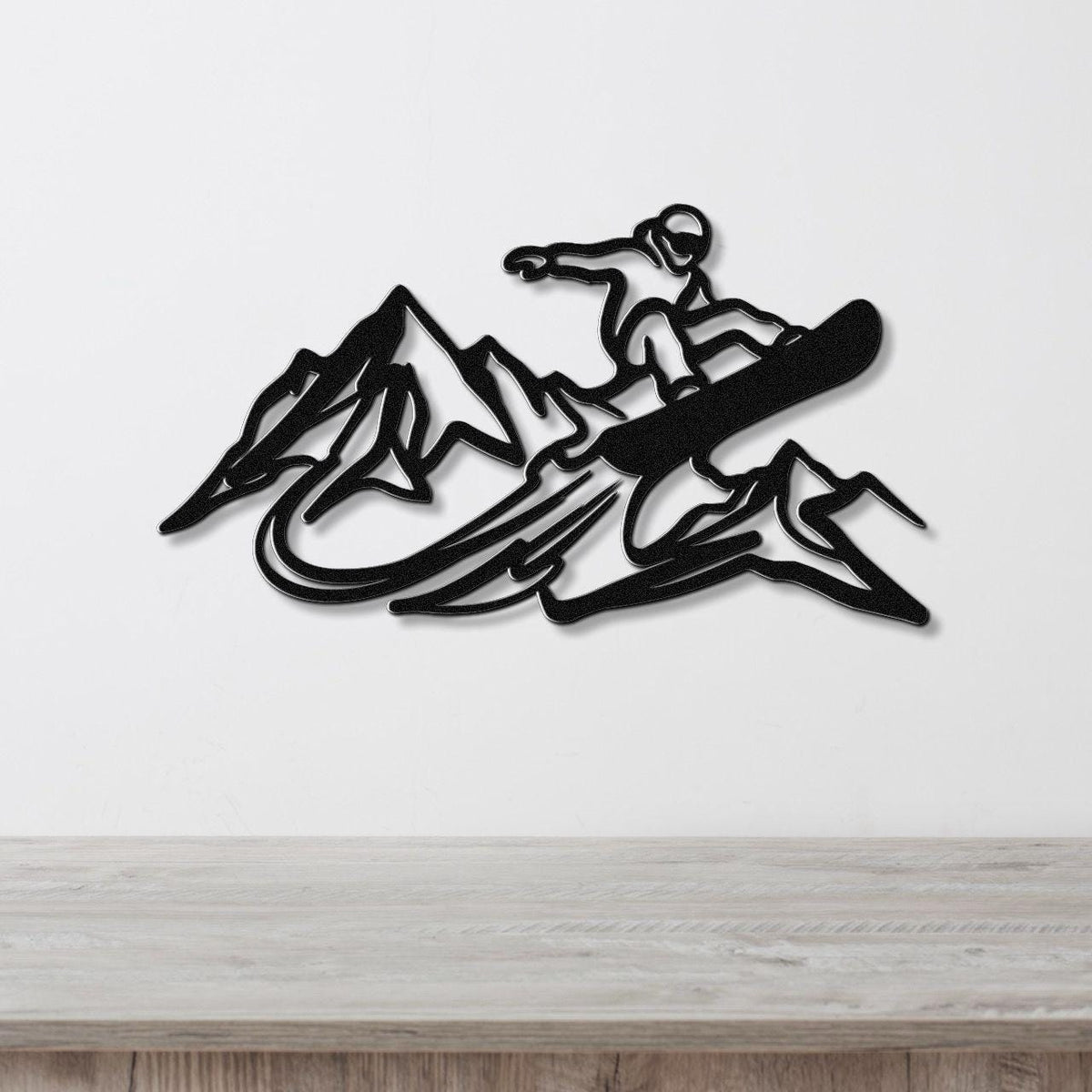 Black metal wall art featuring a snowboarder silhouette above mountain peaks, mounted on a white wall above a wooden counter.