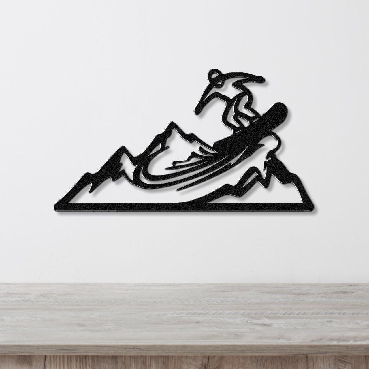 Black metal wall art featuring a snowboarder silhouette mid-air over mountain peaks, mounted on a white wall above a wooden surface.