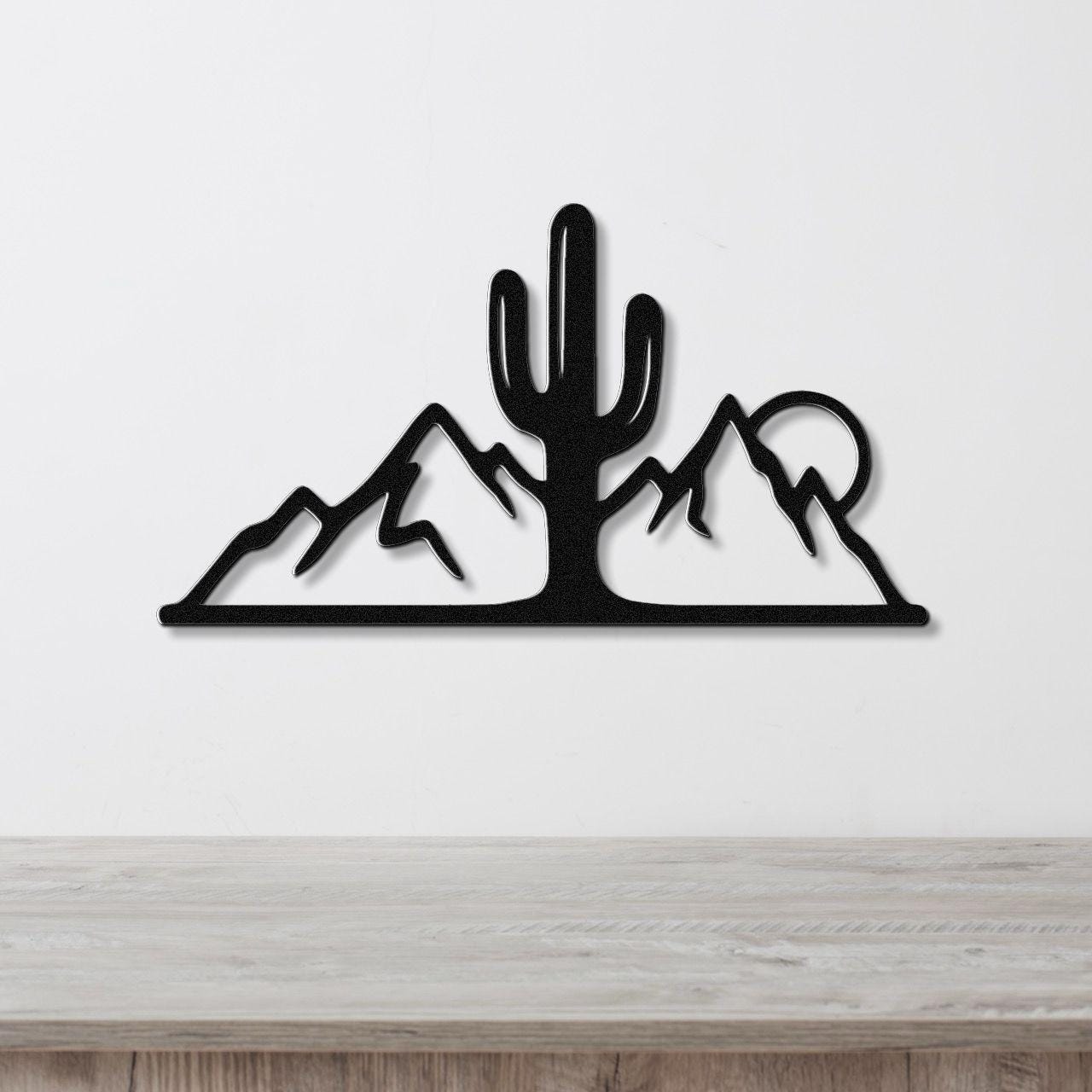 Black metal wall art silhouette of a saguaro cactus and mountain range, mounted on a white wall above a light wood counter.