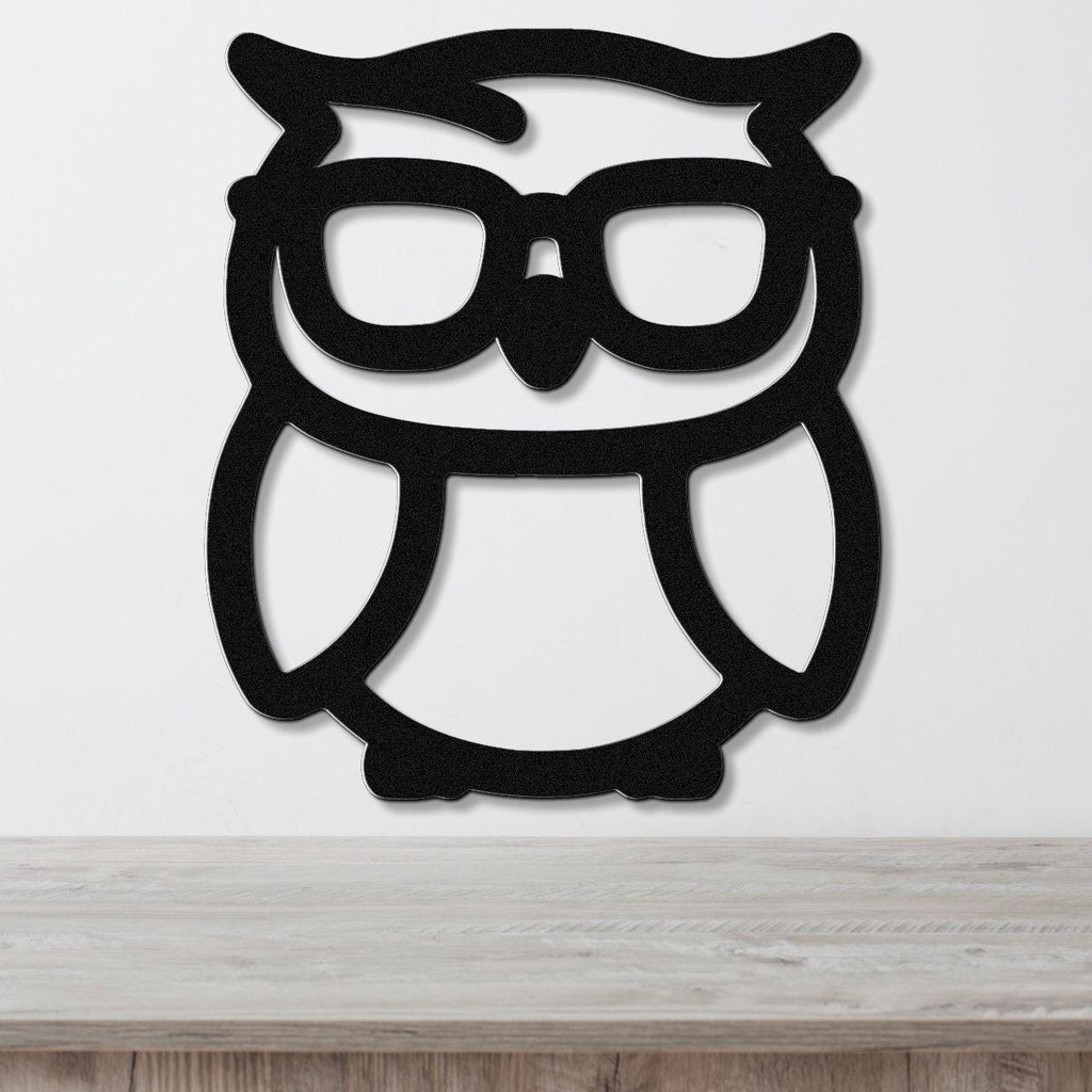Black metal owl wall art with glasses silhouette, mounted on a white wall above a wooden surface.