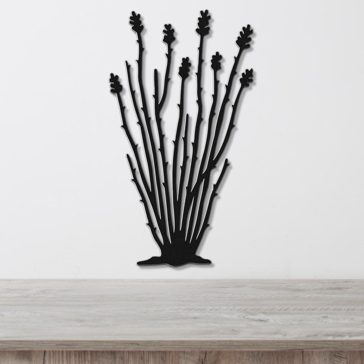 Black metal wall art cutout of an ocotillo plant with multiple spiny stems and leaf clusters, mounted on a white wall above a light wood surface.