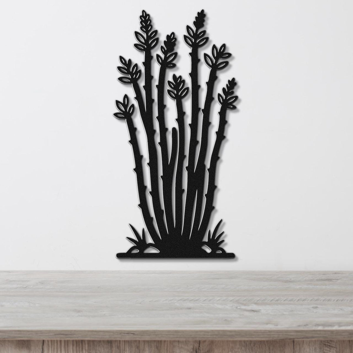Black metal wall art cutout of an ocotillo plant with spiny stems and leaf clusters, mounted on a white wall above a light wood surface.