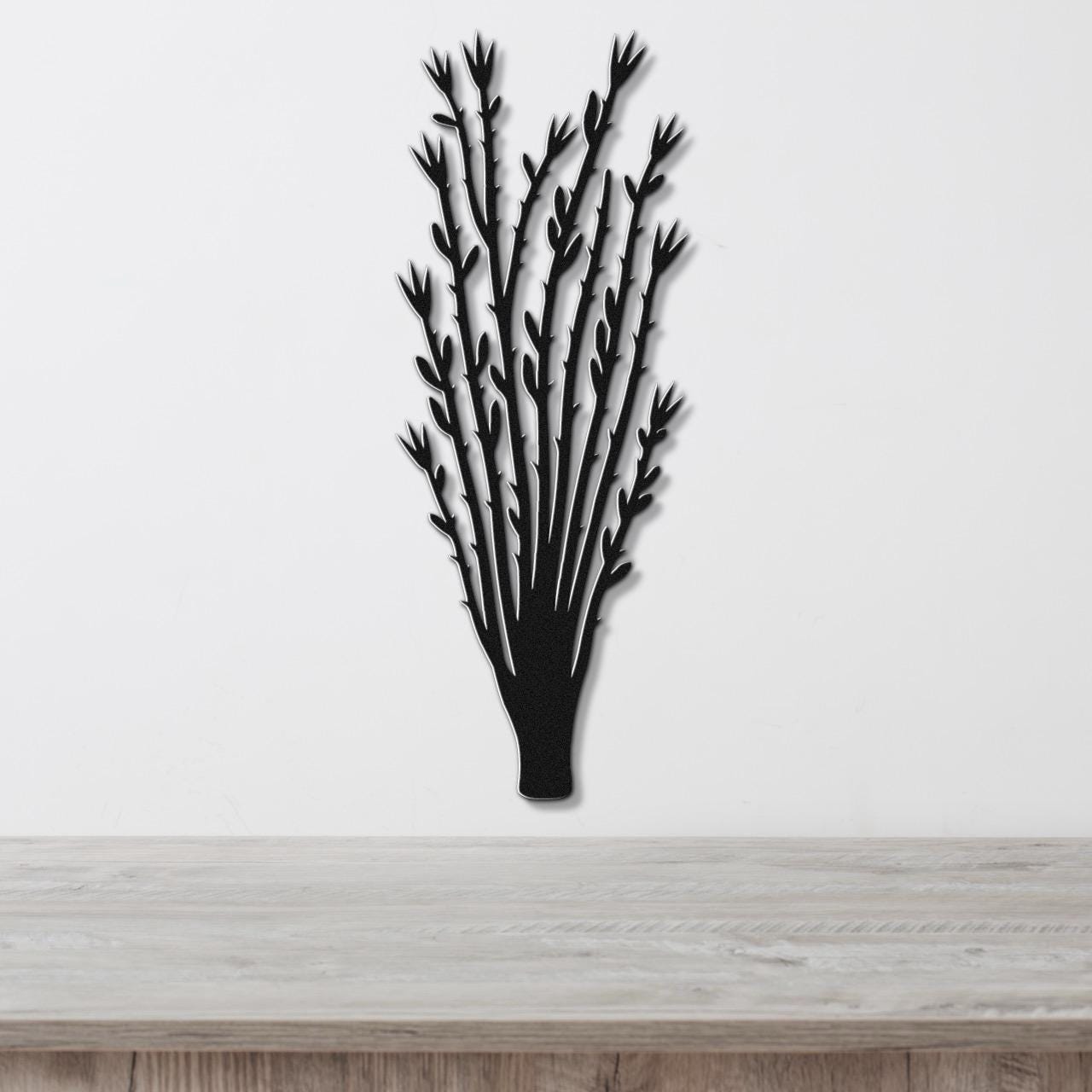 Black metal wall art cutout of an ocotillo plant with branching stems and leaf details, mounted on a white wall above a light wood surface.