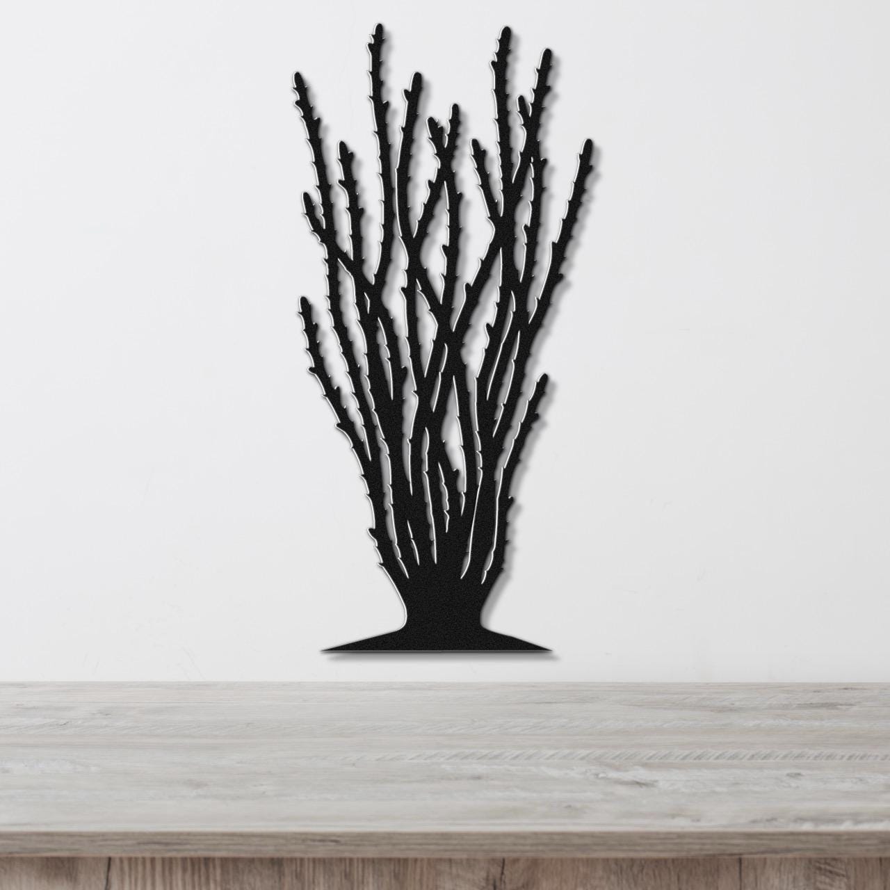 Black metal wall art cutout of an ocotillo plant with branching stems, mounted on a white wall above a light wood counter.