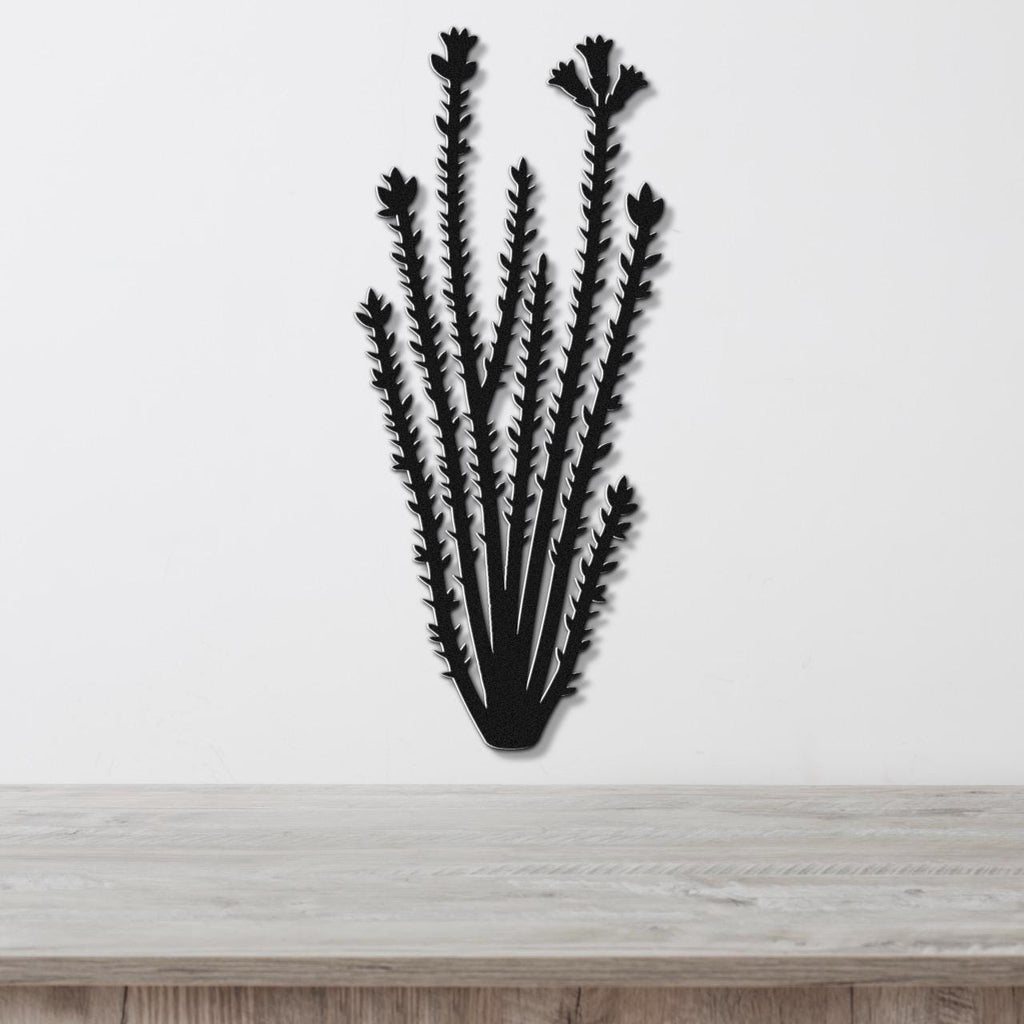 Black metal ocotillo wall art with spiny branches and flower cutouts, mounted on a white wall above a light wood surface.