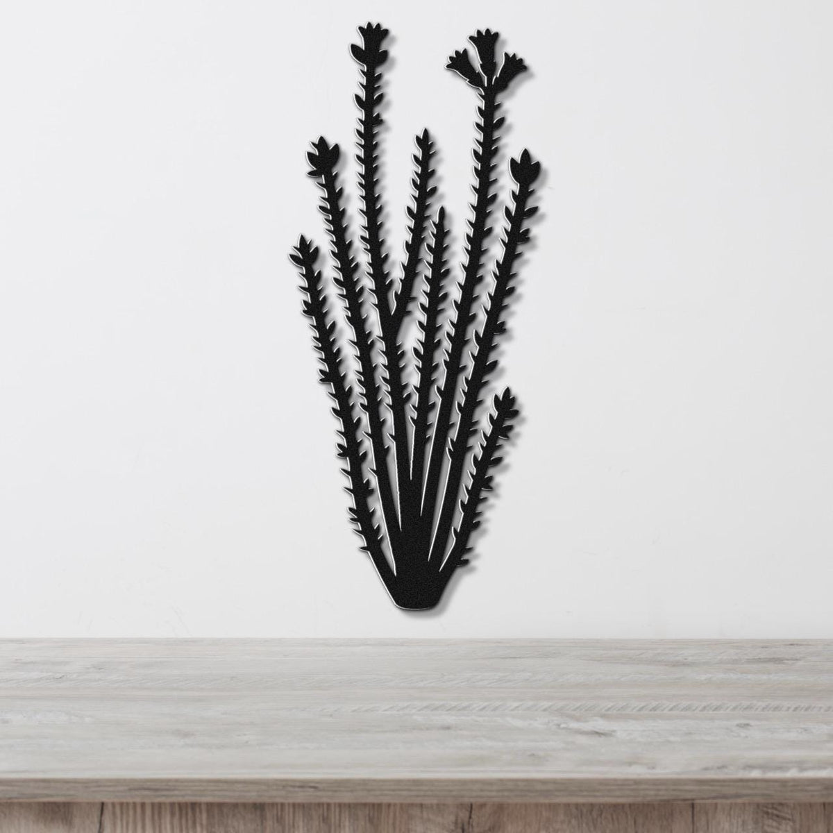 Black metal ocotillo wall art with spiny branches and flower cutouts, mounted on a white wall above a light wood surface.
