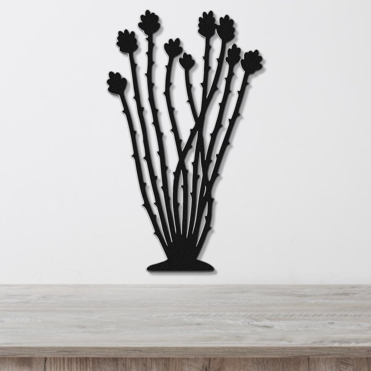 Black metal ocotillo wall art with spiny stems and flower cutouts, mounted on a white wall above a light wood counter.