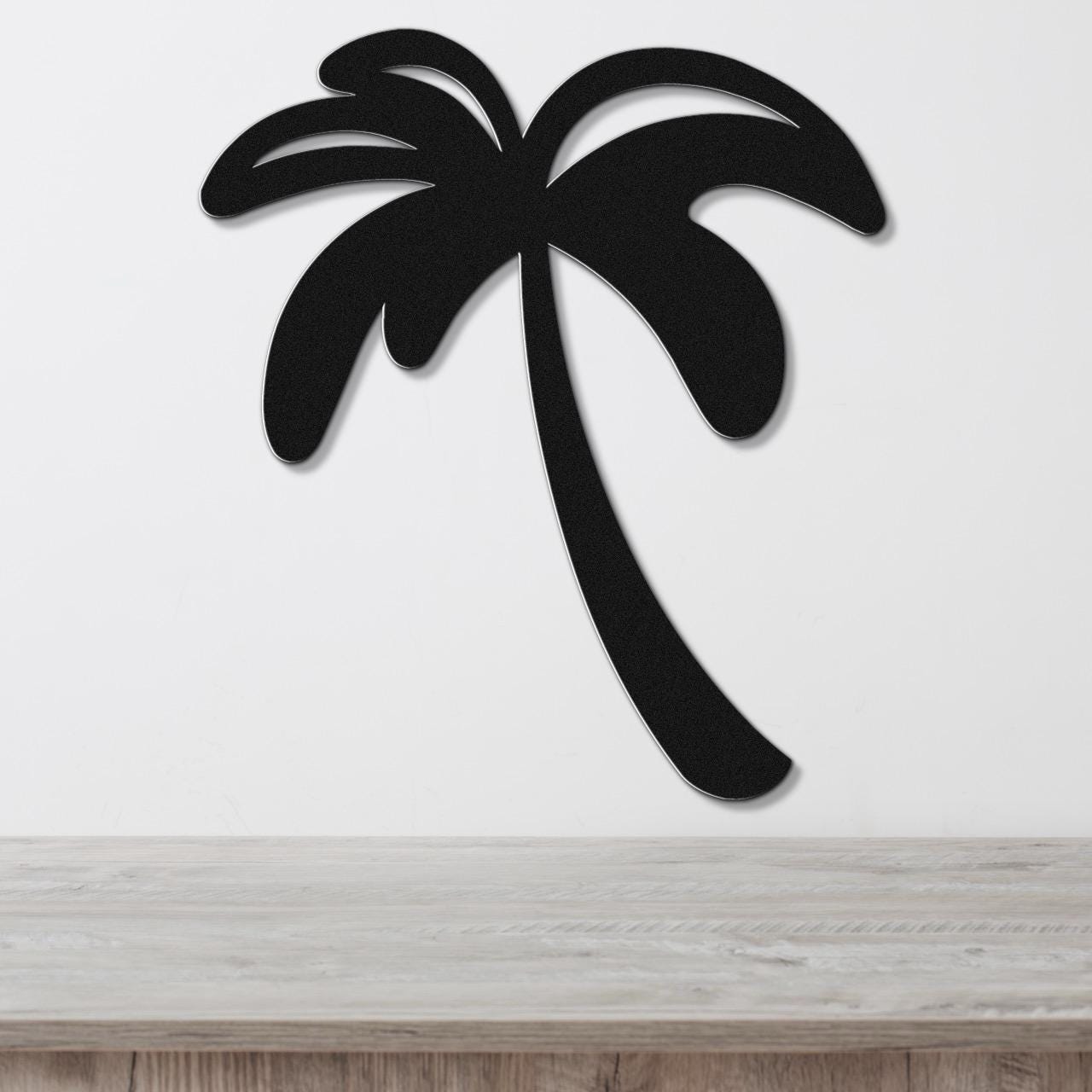 Black metal palm tree wall art with a silhouette cutout design, mounted on a white wall above a light wood surface.