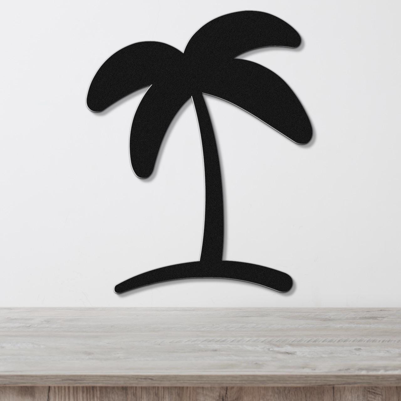 Black metal palm tree wall art with a silhouette design, mounted on a white wall above a light wood surface.