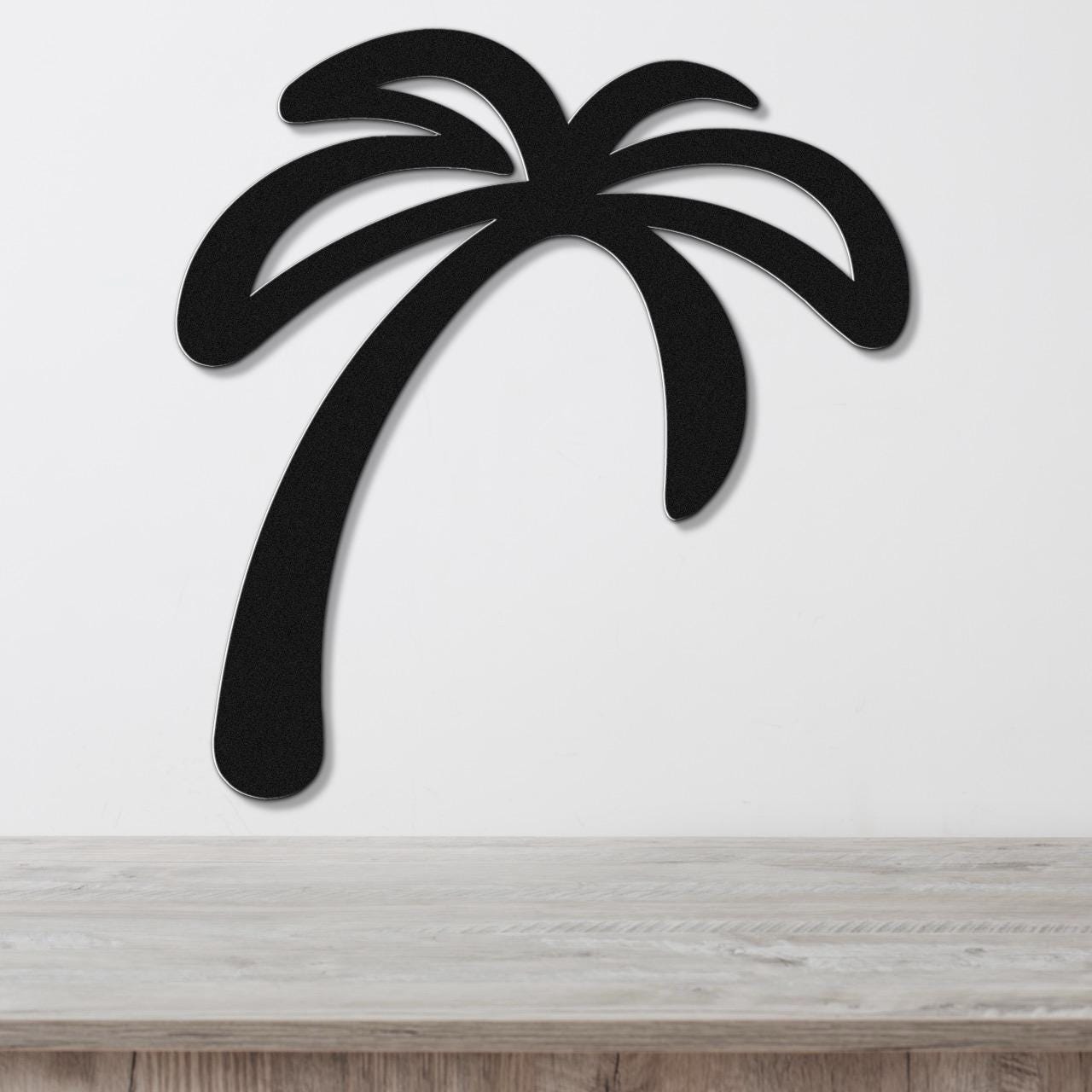 Black metal palm tree wall art with a curved trunk and frond cutouts, mounted on a white wall above a light wood surface.
