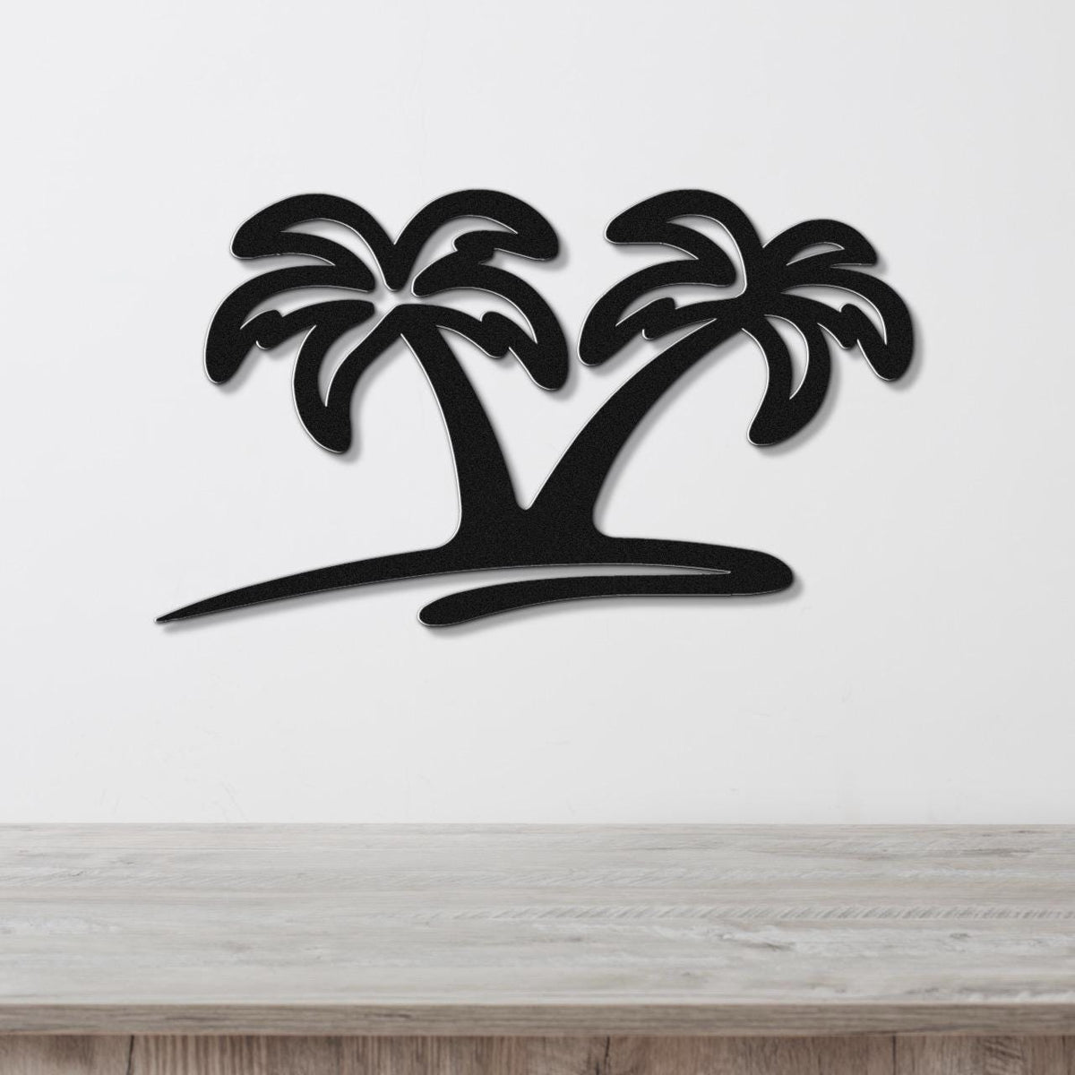 Black metal wall art featuring a silhouette of two palm trees with cutout fronds, mounted on a white wall above a wooden surface.