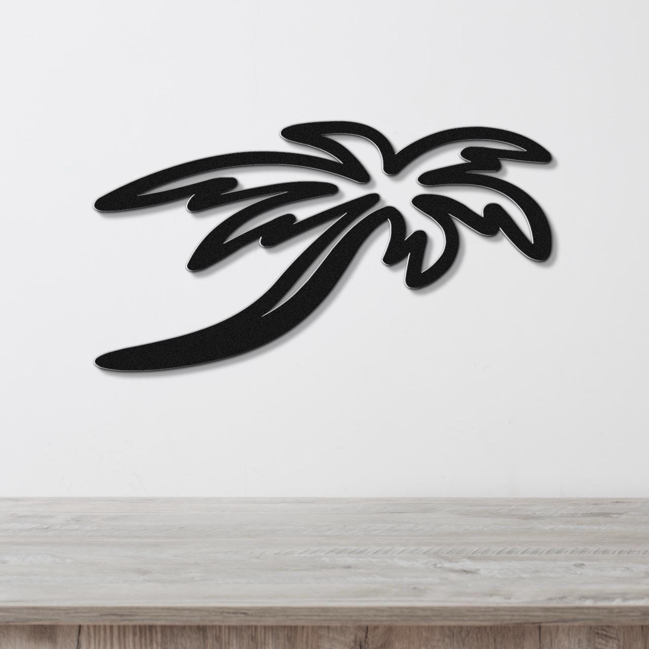 Black metal palm tree wall art with layered frond cutouts, mounted on a white wall above a light wood surface.
