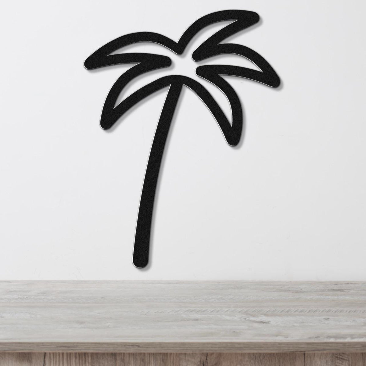 Black metal palm tree wall art with leaf cutouts, mounted on a white wall above a light wood surface.