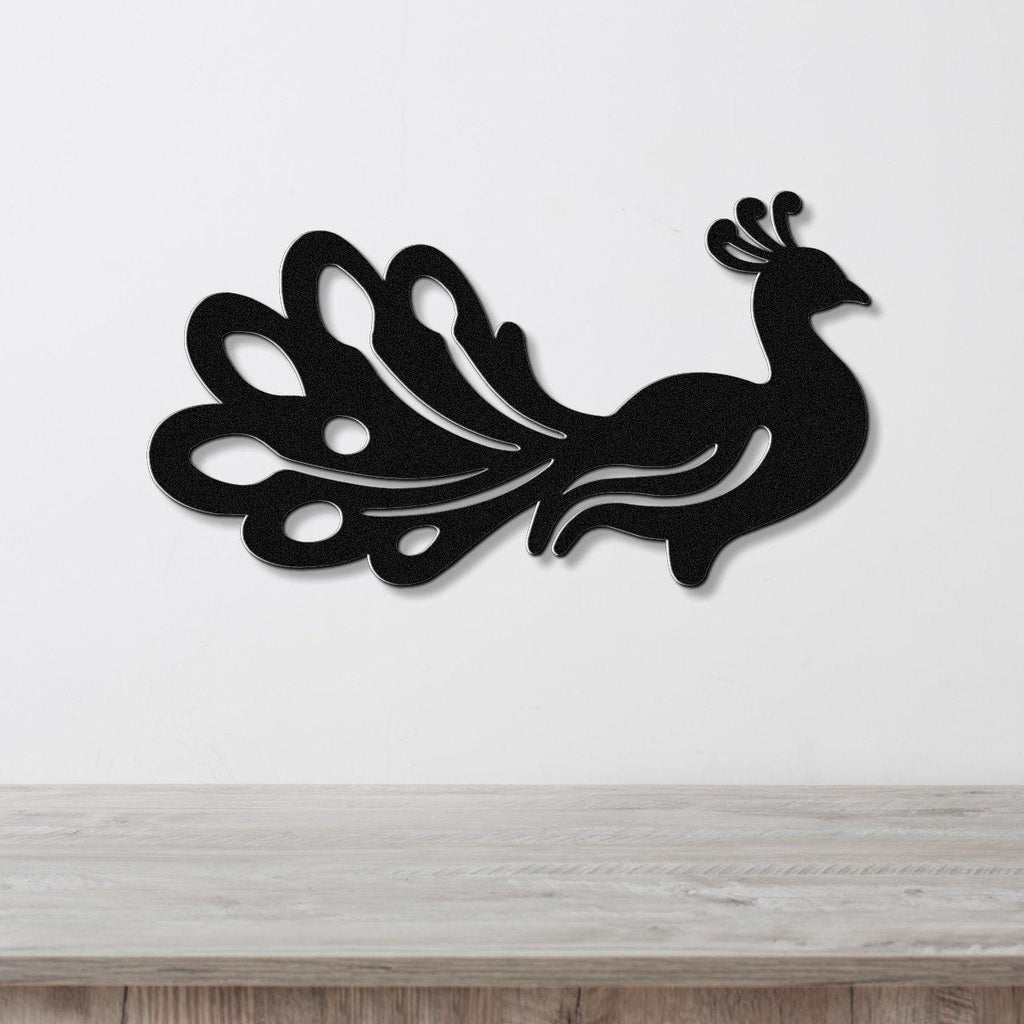 Black metal peacock wall art with a silhouette design and cutout tail feathers, mounted on a white wall above a wooden surface.