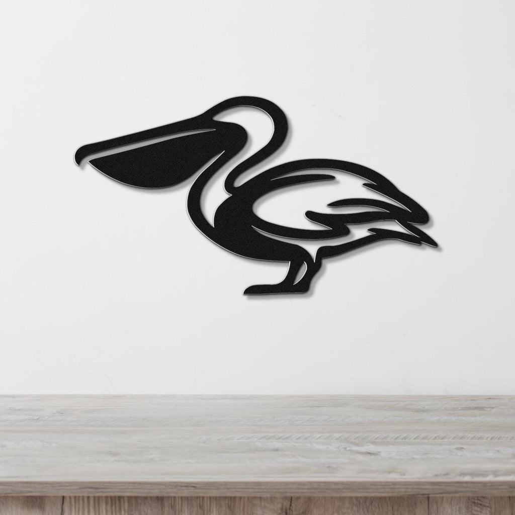 Black metal pelican wall art with a cutout silhouette design, mounted on a white wall above a light wood surface.