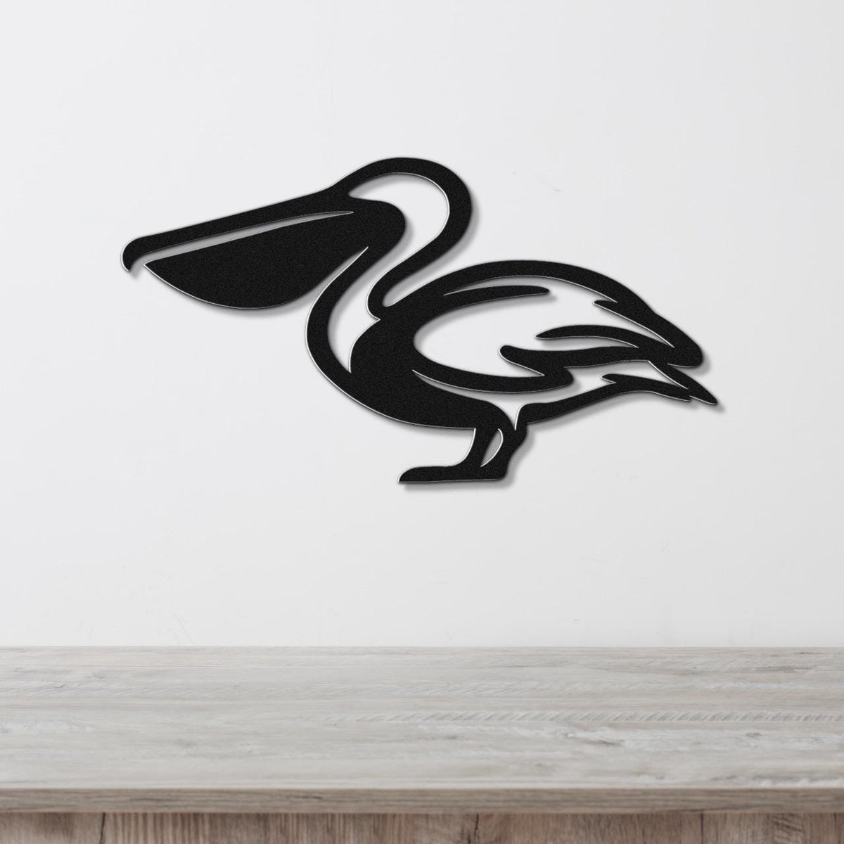 Black metal pelican wall art with a cutout silhouette design, mounted on a white wall above a light wood surface.