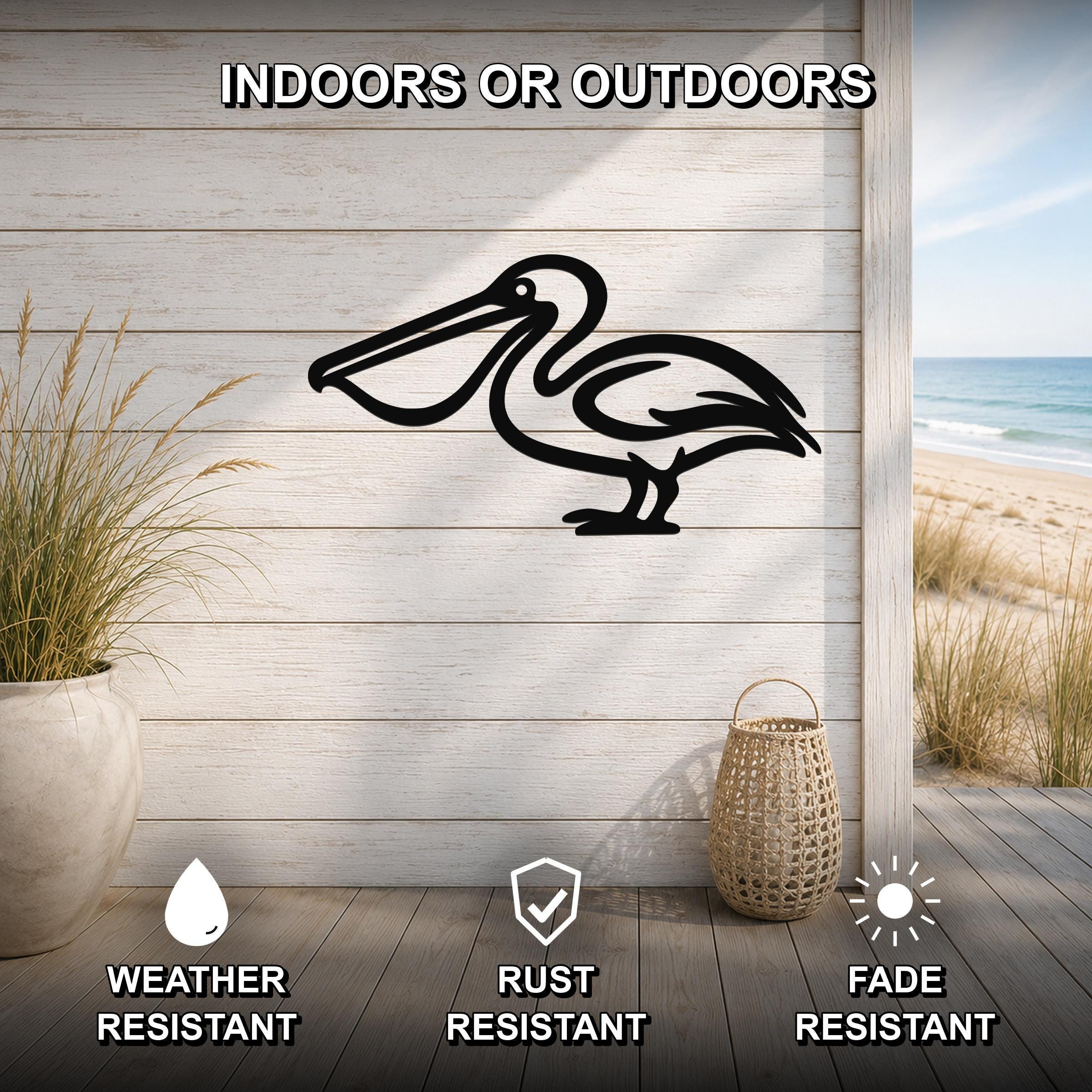 Black metal pelican wall art silhouette mounted on a light wood plank wall, displayed on a patio with a beach view, weather resistant, rust resistant, and fade resistant.
