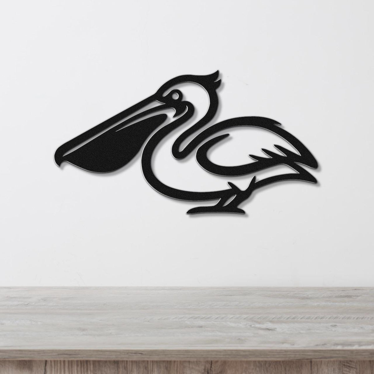 Black metal pelican wall art with a cutout silhouette design, mounted on a white wall above a light wood surface.
