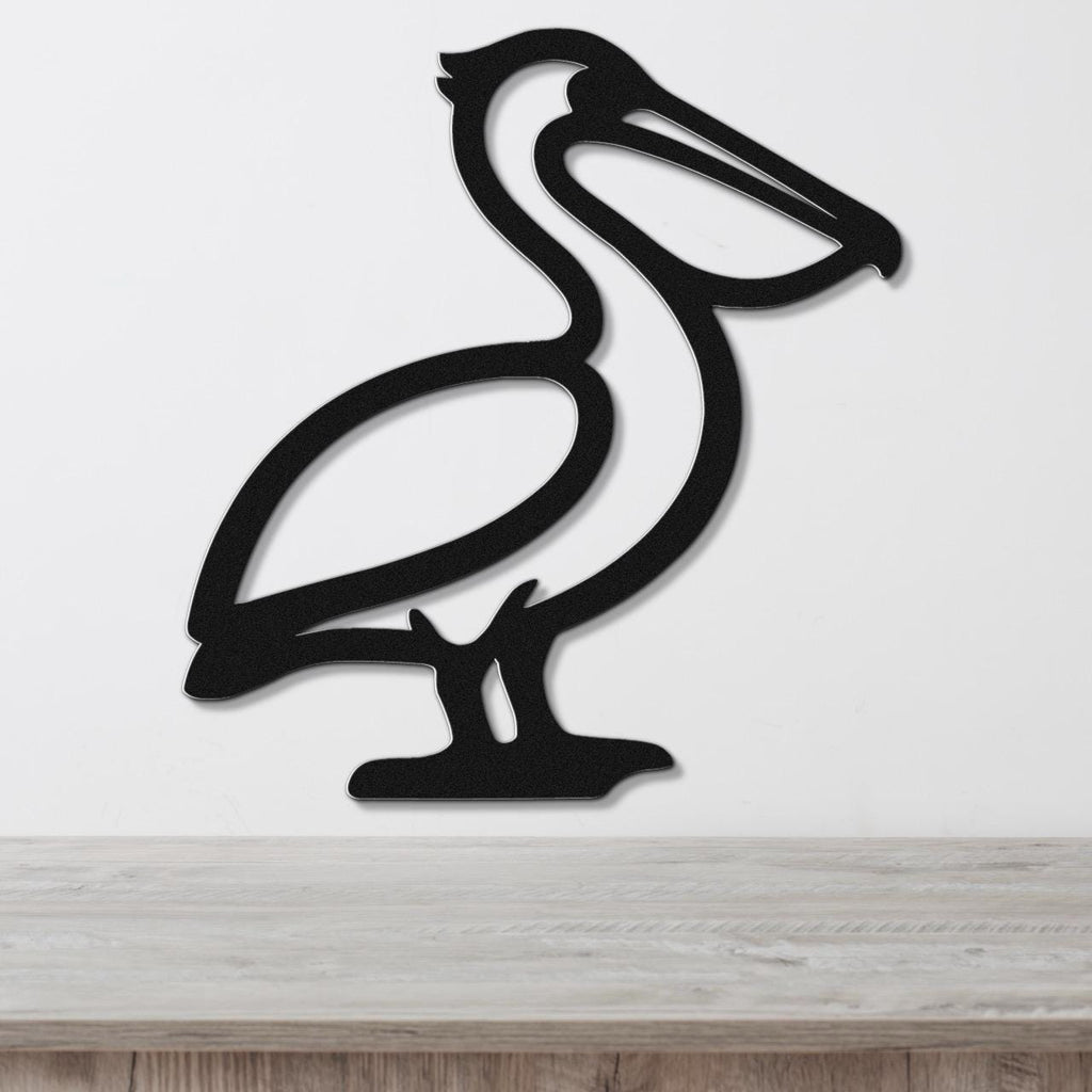 Black metal pelican wall art with a cutout silhouette design, mounted on a white wall above a light wood surface.
