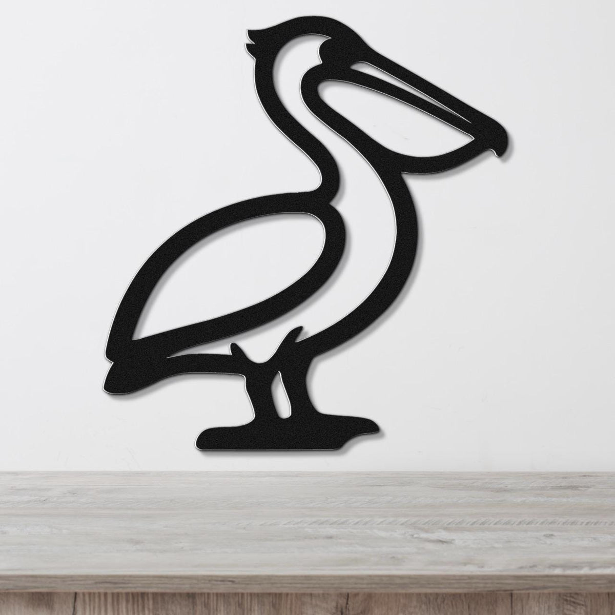 Black metal pelican wall art with a cutout silhouette design, mounted on a white wall above a light wood surface.