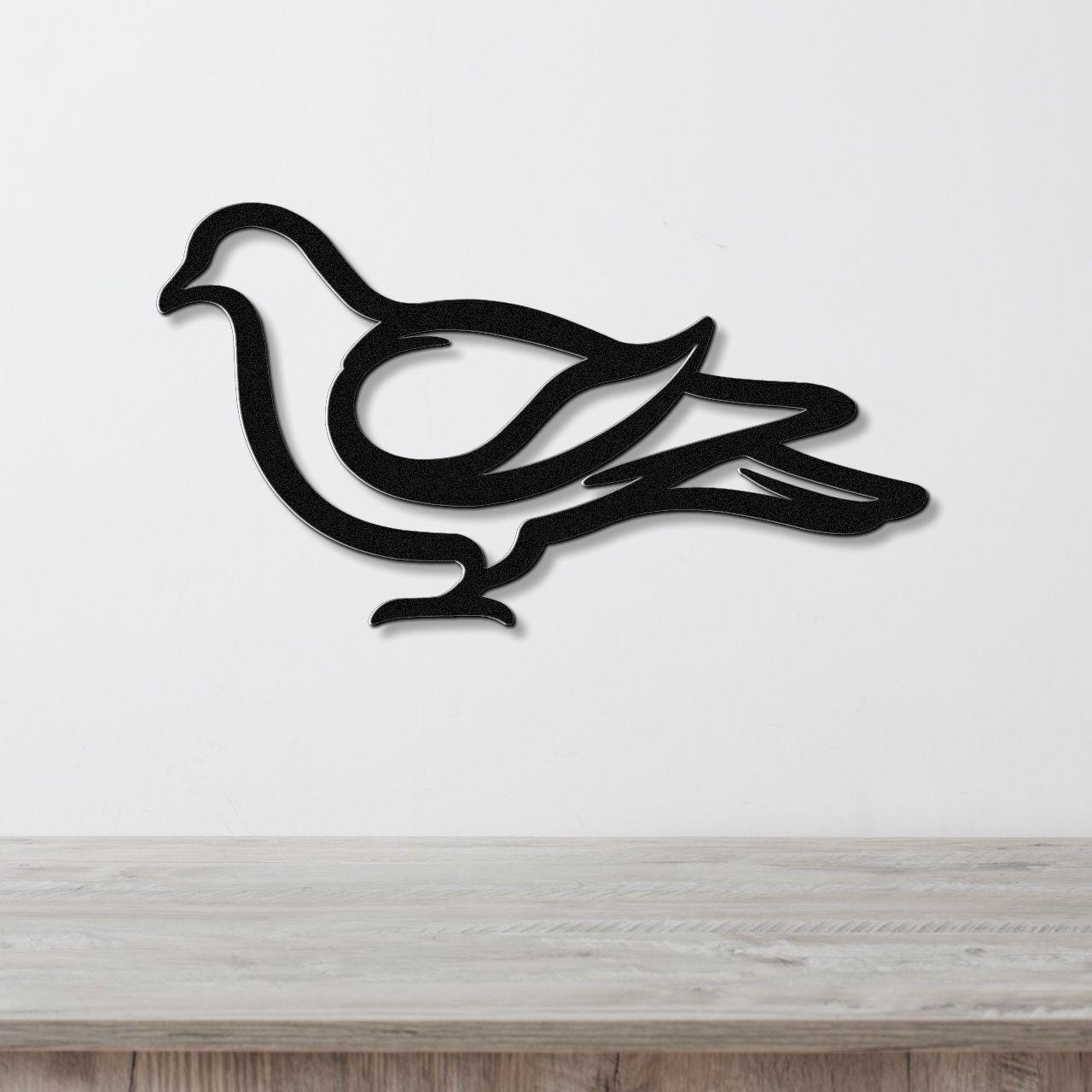 Black metal pigeon wall art with a minimalist silhouette design, mounted on a white wall above a light wood surface.