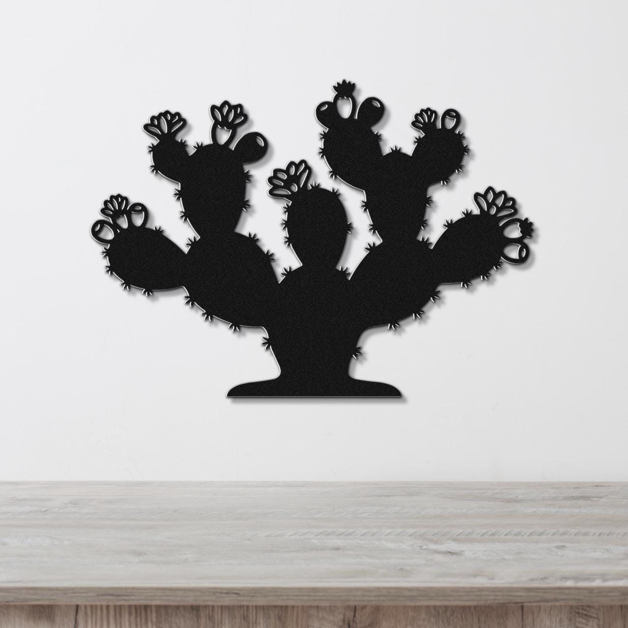 Black metal cactus wall art with flower and spine cutouts, mounted on a white wall above a wooden counter.