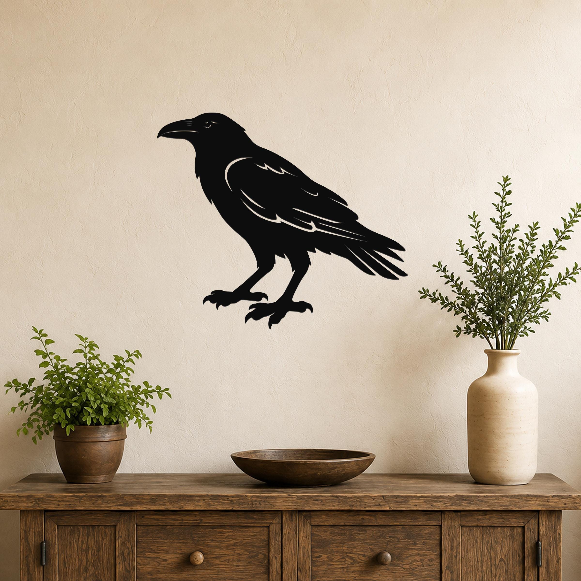 Black metal raven wall art silhouette with detailed feather cutouts, mounted on a beige wall above a wooden console table with potted plants.