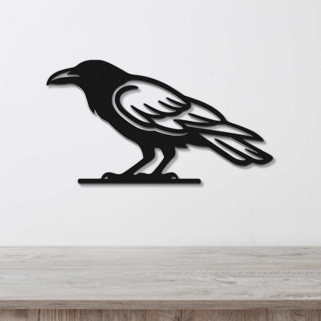 Black metal raven wall art with cutout wing and tail details, mounted on a white wall above a light wood surface.