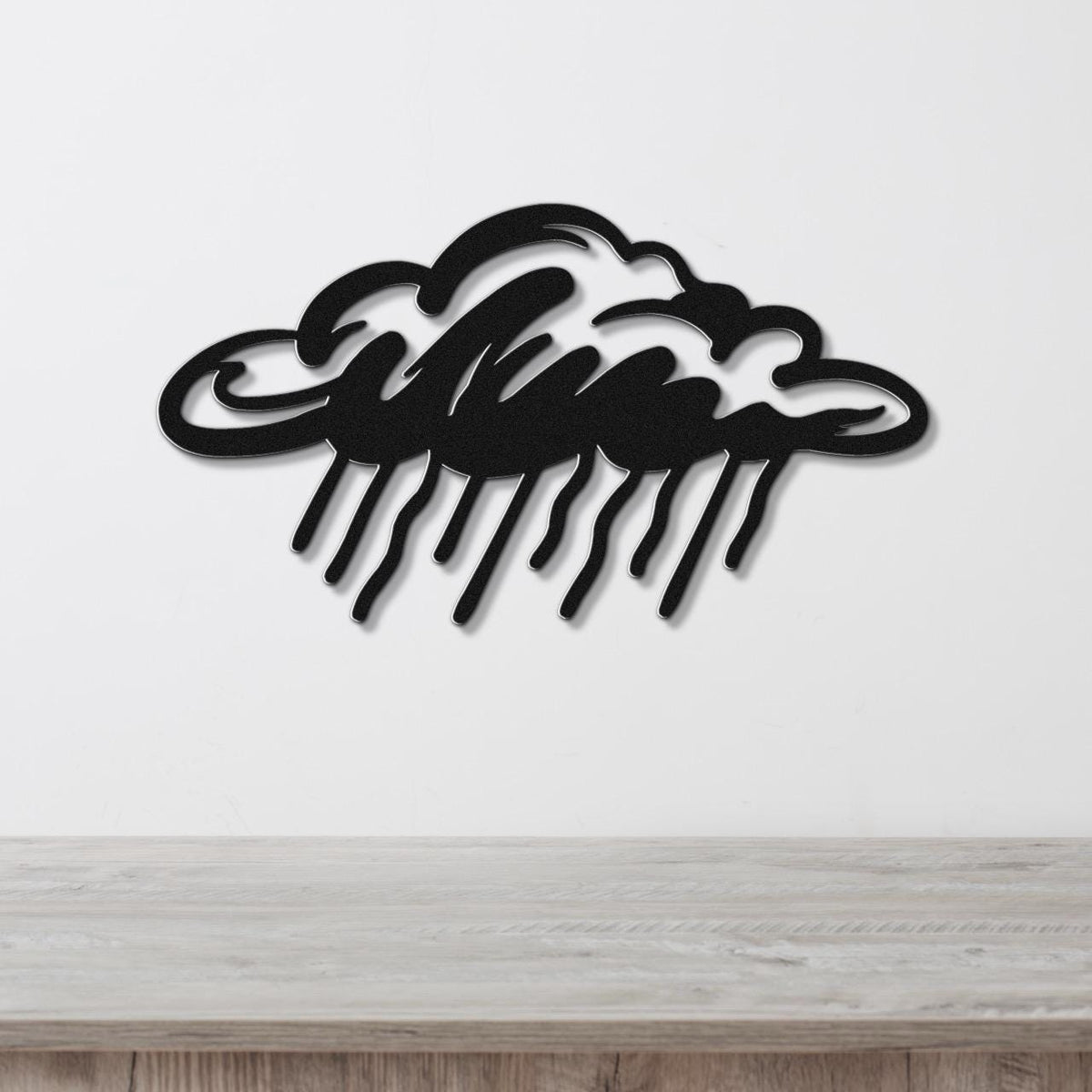 Black metal wall art in a cloud shape with raindrop cutouts, mounted on a white wall above a wooden surface.