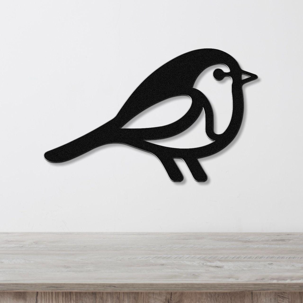 Black metal robin wall art with a cutout silhouette design, mounted on a white wall above a light wood surface.