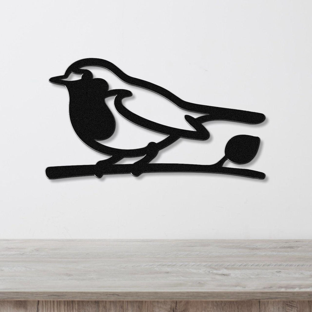 Black metal robin wall art silhouette perched on a branch, mounted on a white wall above a wooden surface.