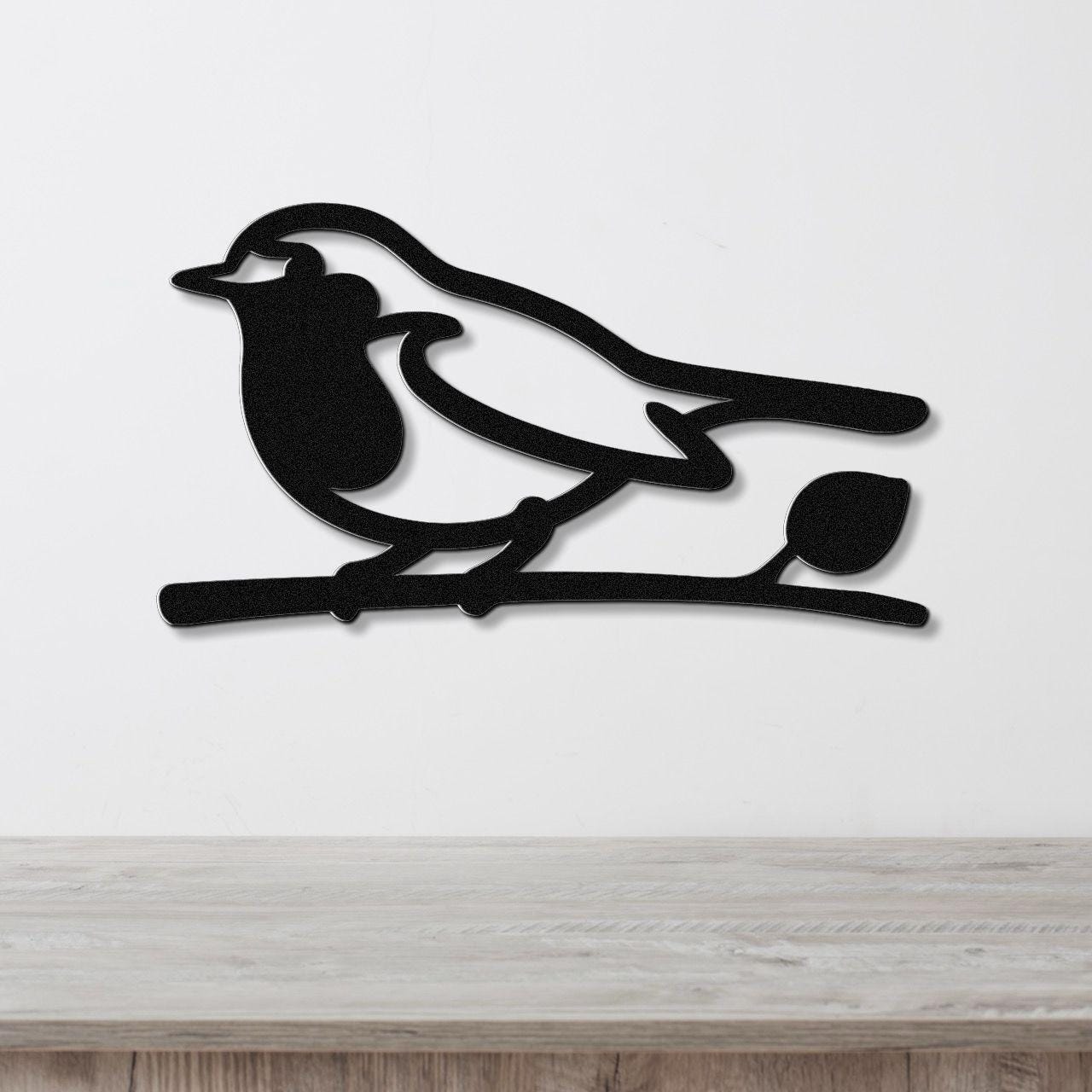 Black metal robin wall art silhouette perched on a branch, mounted on a white wall above a wooden surface.