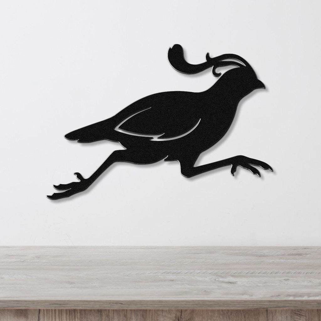 Black metal quail wall art in a running silhouette with a curved crest, mounted on a white wall above a light wood counter.