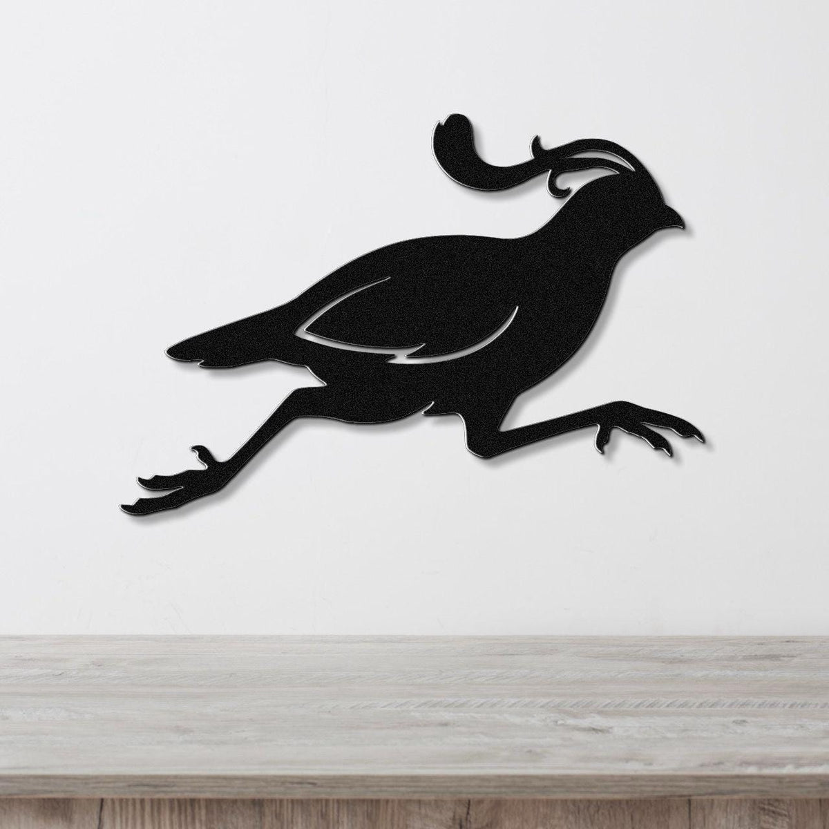 Black metal quail wall art in a running silhouette with a curved crest, mounted on a white wall above a light wood counter.