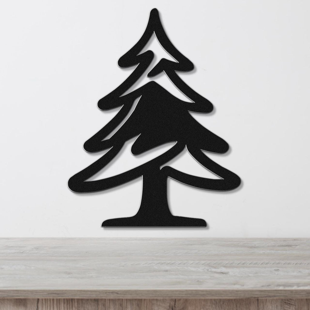 Black metal pine tree wall art with layered branch cutouts, mounted on a white wall above a light wood surface.