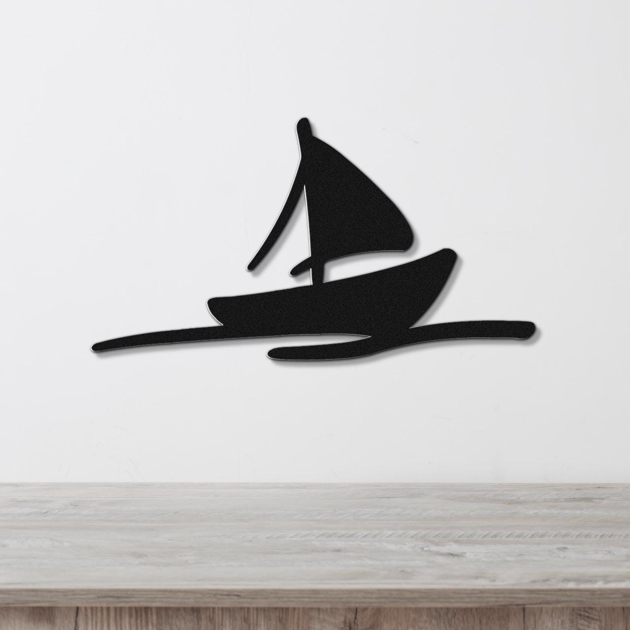Black metal sailboat wall art with a silhouette design, mounted on a white wall above a light wood surface.