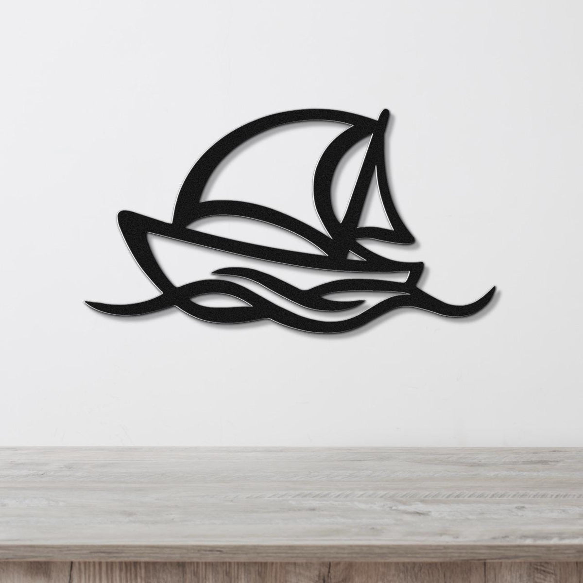 Black metal wall art silhouette of a sailboat with wave cutouts, mounted on a white wall above a wooden surface.