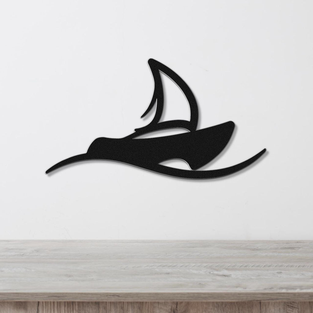 Black metal wall art in the silhouette of a sailboat with a cutout sail, mounted on a white wall above a light wood surface.