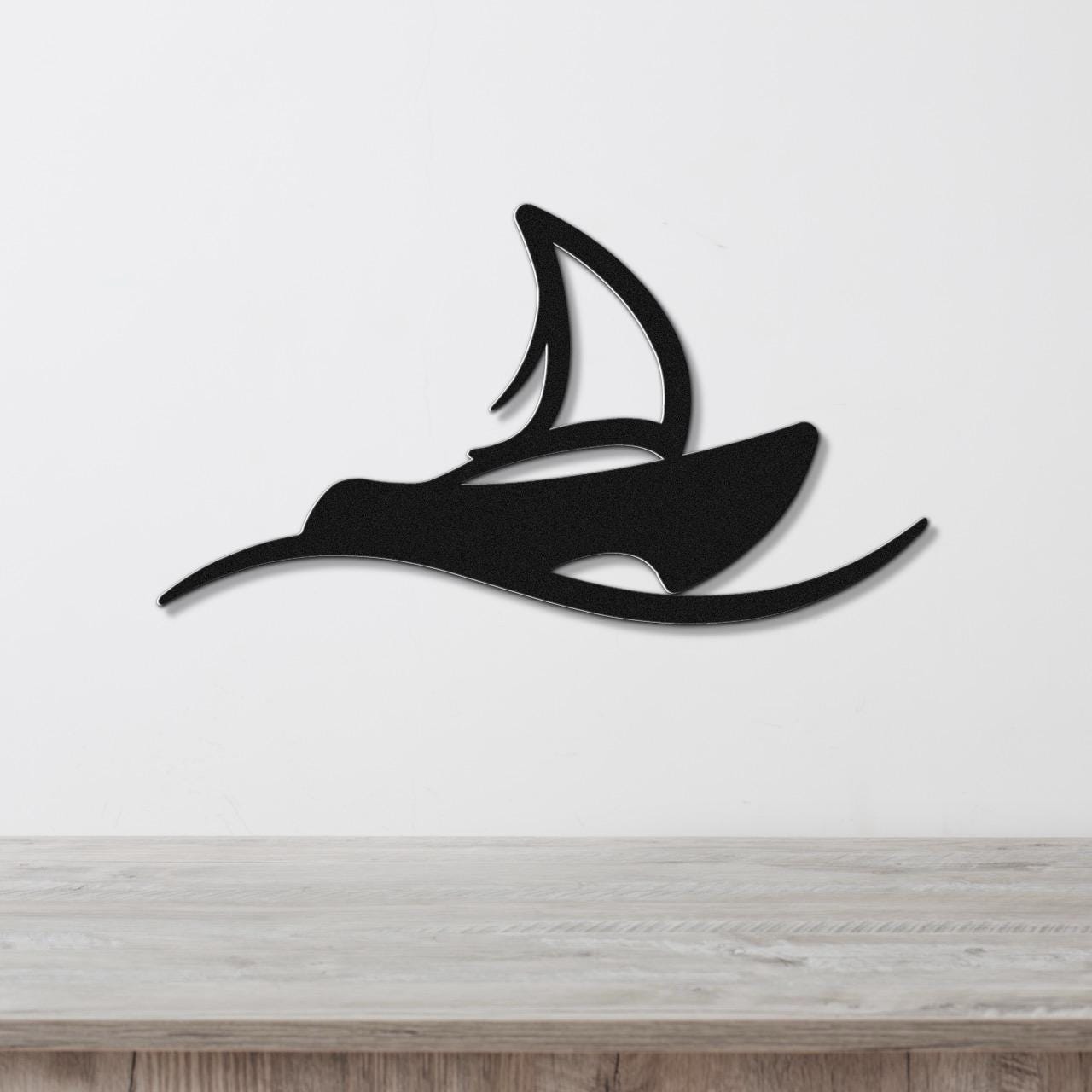Black metal wall art in the silhouette of a sailboat with a cutout sail, mounted on a white wall above a light wood surface.