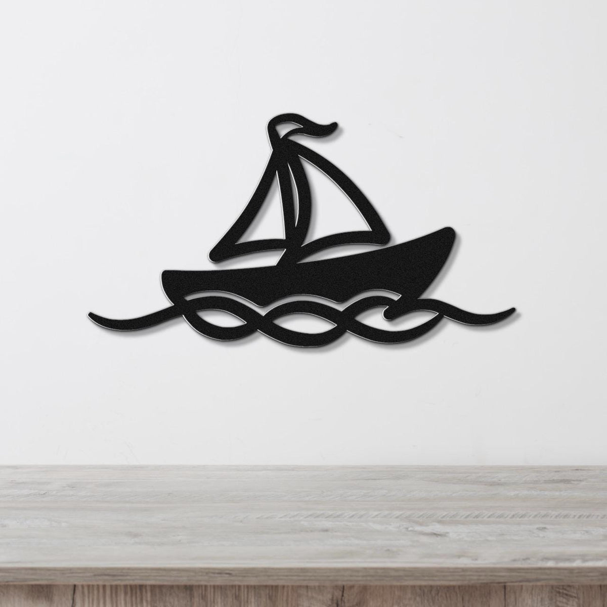 Black metal sailboat wall art with wave cutouts, mounted on a white wall above a light wood surface.