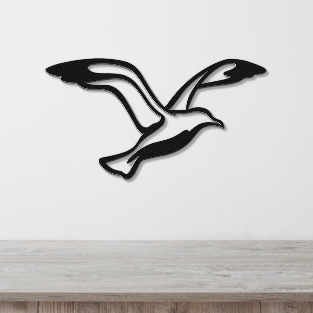 Black metal seagull wall art with flowing wing cutouts, mounted on a white wall above a light wood countertop.