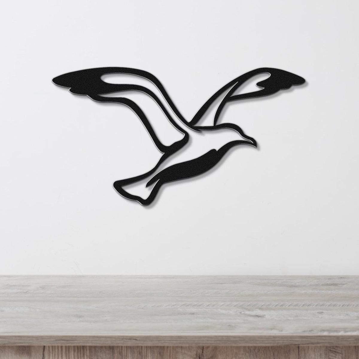 Black metal seagull wall art with flowing wing cutouts, mounted on a white wall above a light wood countertop.